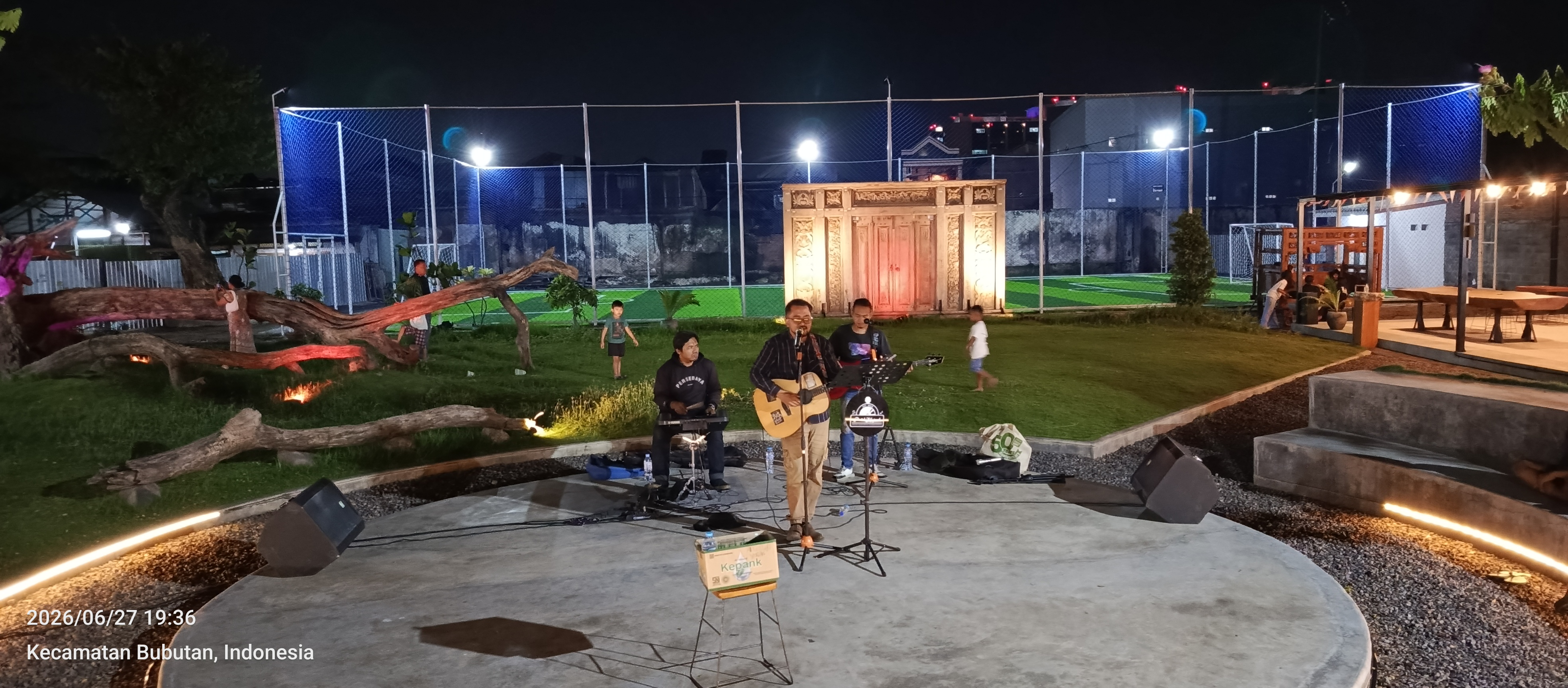 A band playing live on the amphitheatre stage at Dupak 36 at night, with the floodlit soccer pitch behind them.