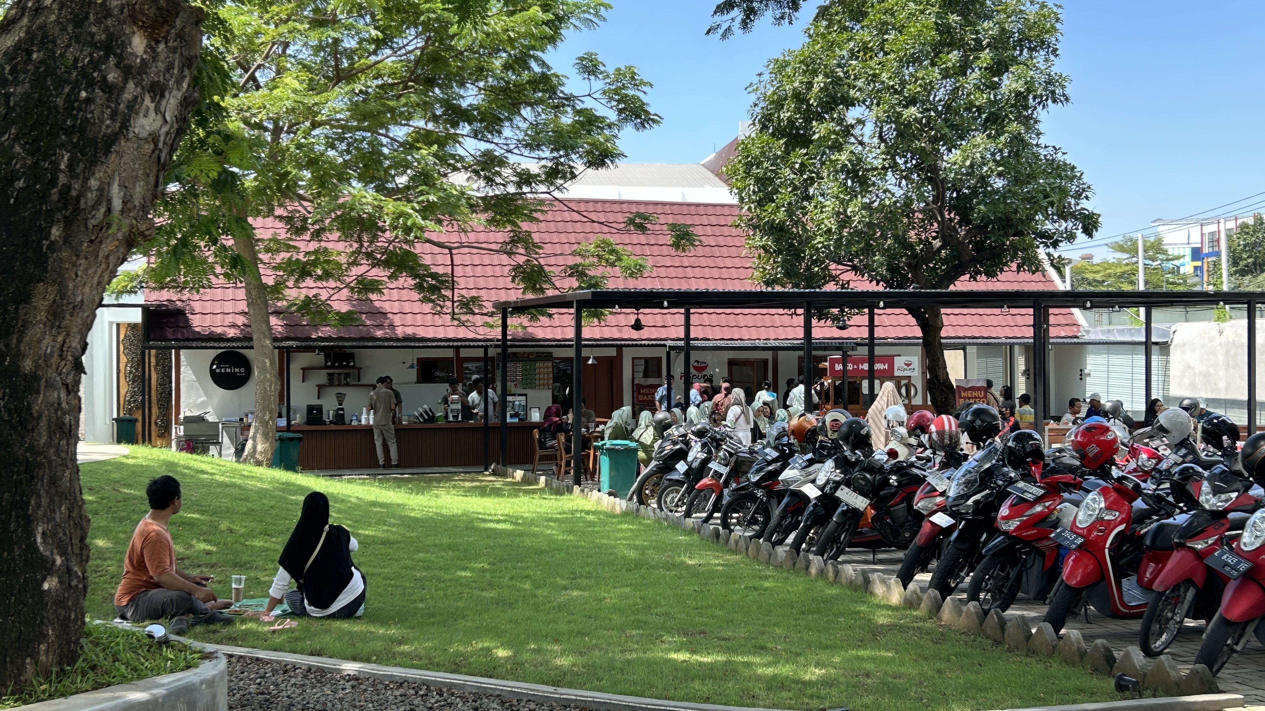 Visitors sitting on the shaded lawn at Dupak 36, with the tenant units and motorcycle parking behind them.