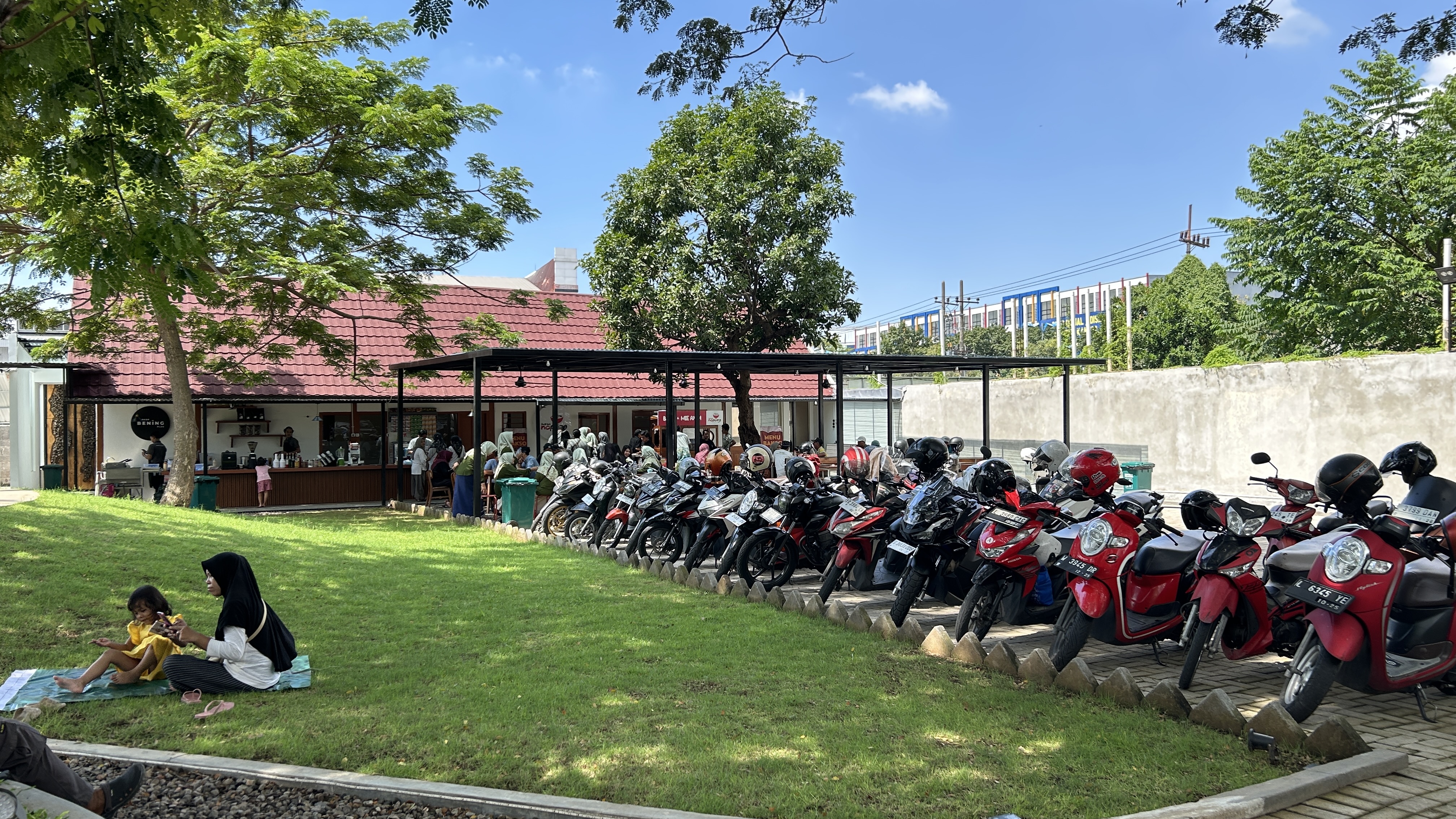 Visitors queueing at the food tenant units at Dupak 36, with motorcycle parking alongside the lawn.